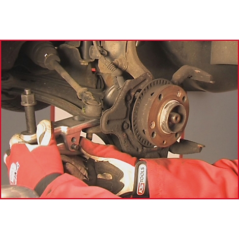 Person in roter Kleidung und Handschuhen montiert an einem Autoreifen. Werkzeug und Autoteile sind zu sehen.